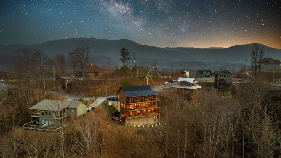 Dream Catcher Chalet glowing at twilight under the Milky Way with the Smoky Mountains behind